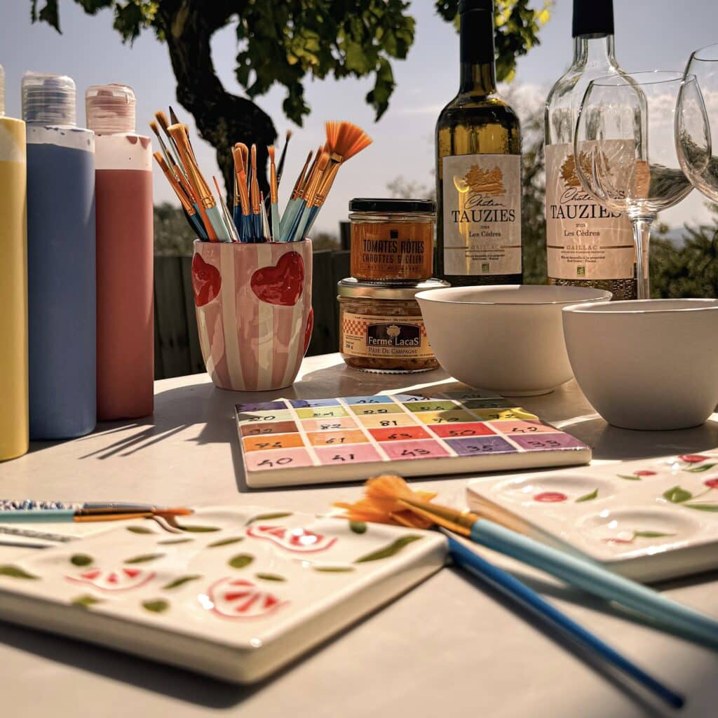 Table d'atelier céramique avec pinceaux, peintures, vins du Château de Tauziès et tapas